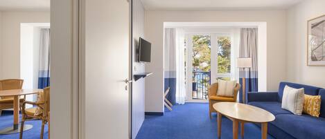 Habitación de hotel con alfombra azul, un sofá, una mesa y un televisor montado en la pared.