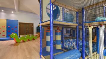 Un espace de jeux avec une enceinte grillagée, une structure de jeu en forme de serpent vert et un tapis de jeu bleu et beige.