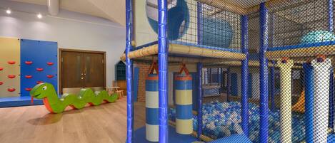 Ein Spielbereich mit einem durch ein Netz gesicherten Bereich, einer Spielkonstruktion in Form einer grünen Schlange und einer blau-beigen Spielmatte.