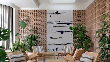 Ett modernt inomhusutrymme med en geometrisk väggdesign, en central sittgrupp med möbler i rotting och ett stort, abstrakt konstverk.