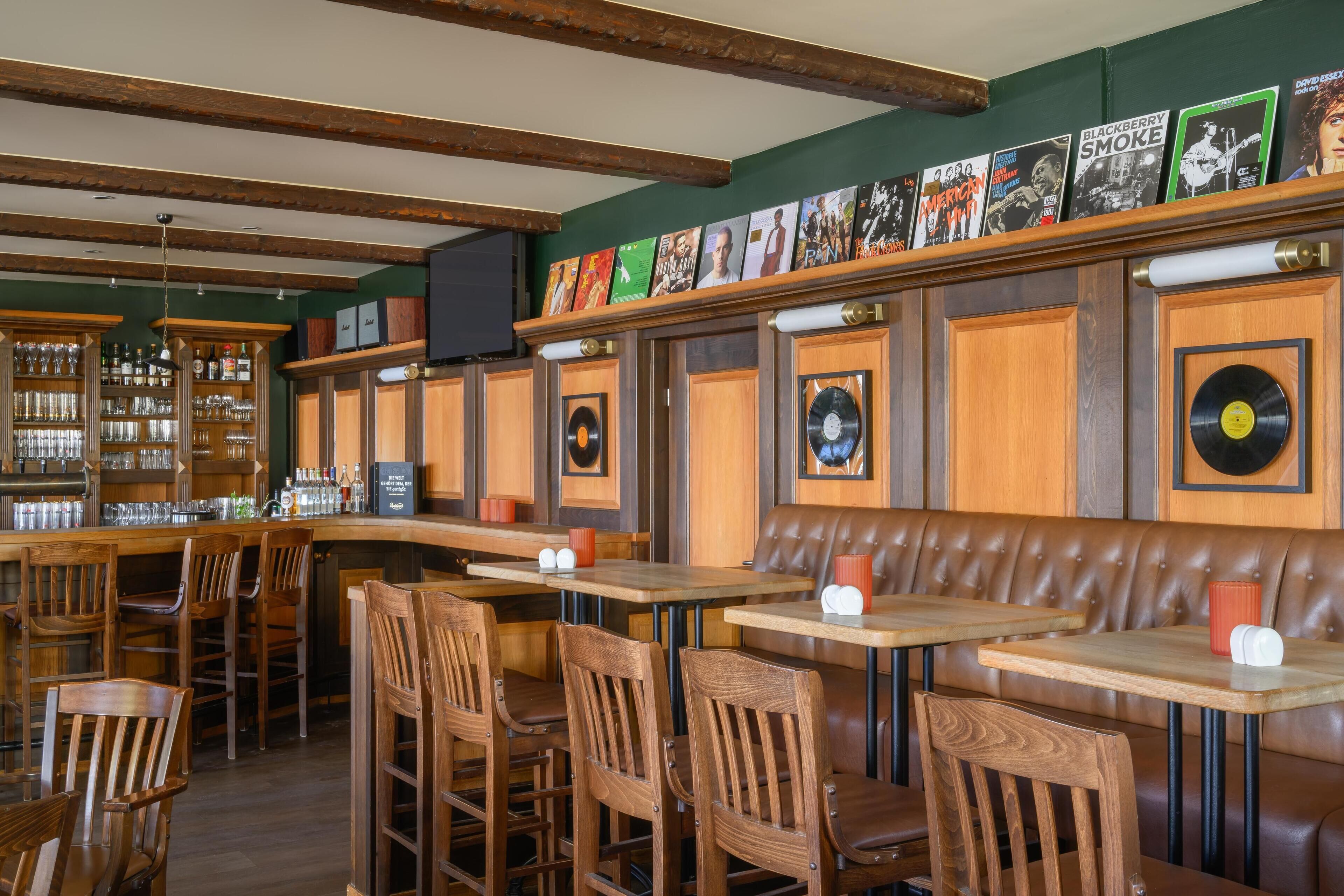 Un restaurante con mobiliario de madera, una zona de bar y decoración de pared que incluye discos de vinilo y fotografías enmarcadas.