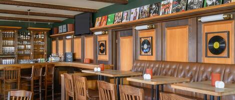 Un restaurant amb mobiliari de fusta, zona de bar i decoració mural que inclou discos de vinil i quadres emmarcats.