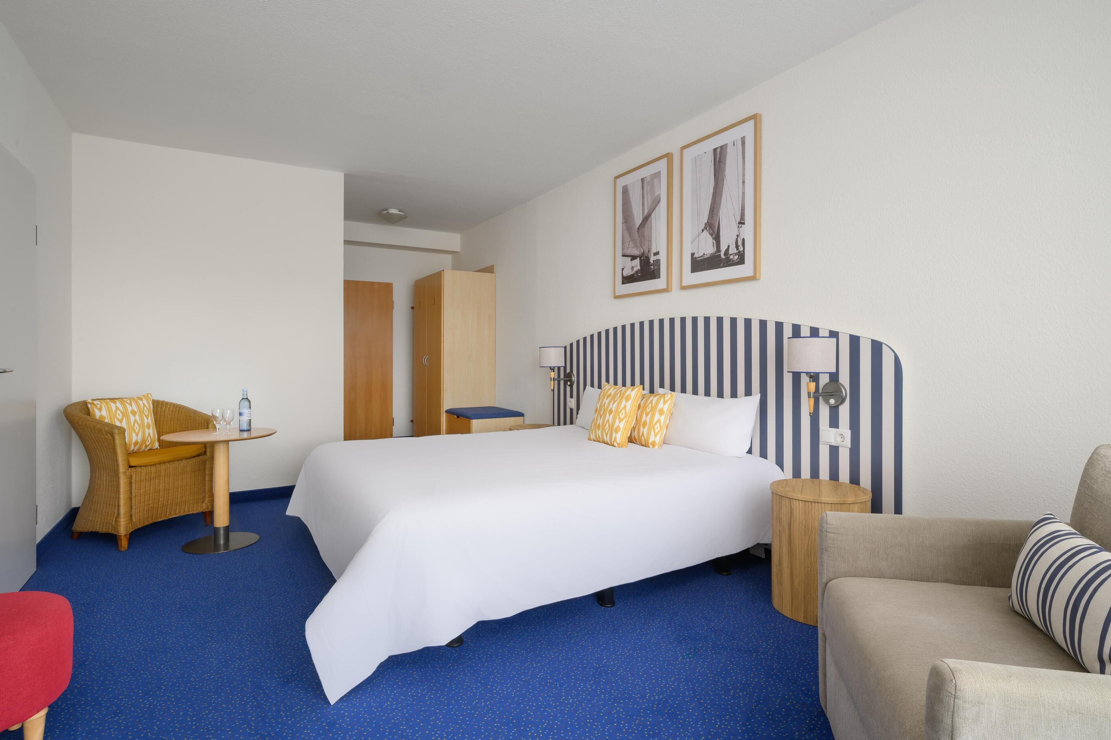 A hotel room with a large bed, a sofa, a chair, a small table, and a nightstand.