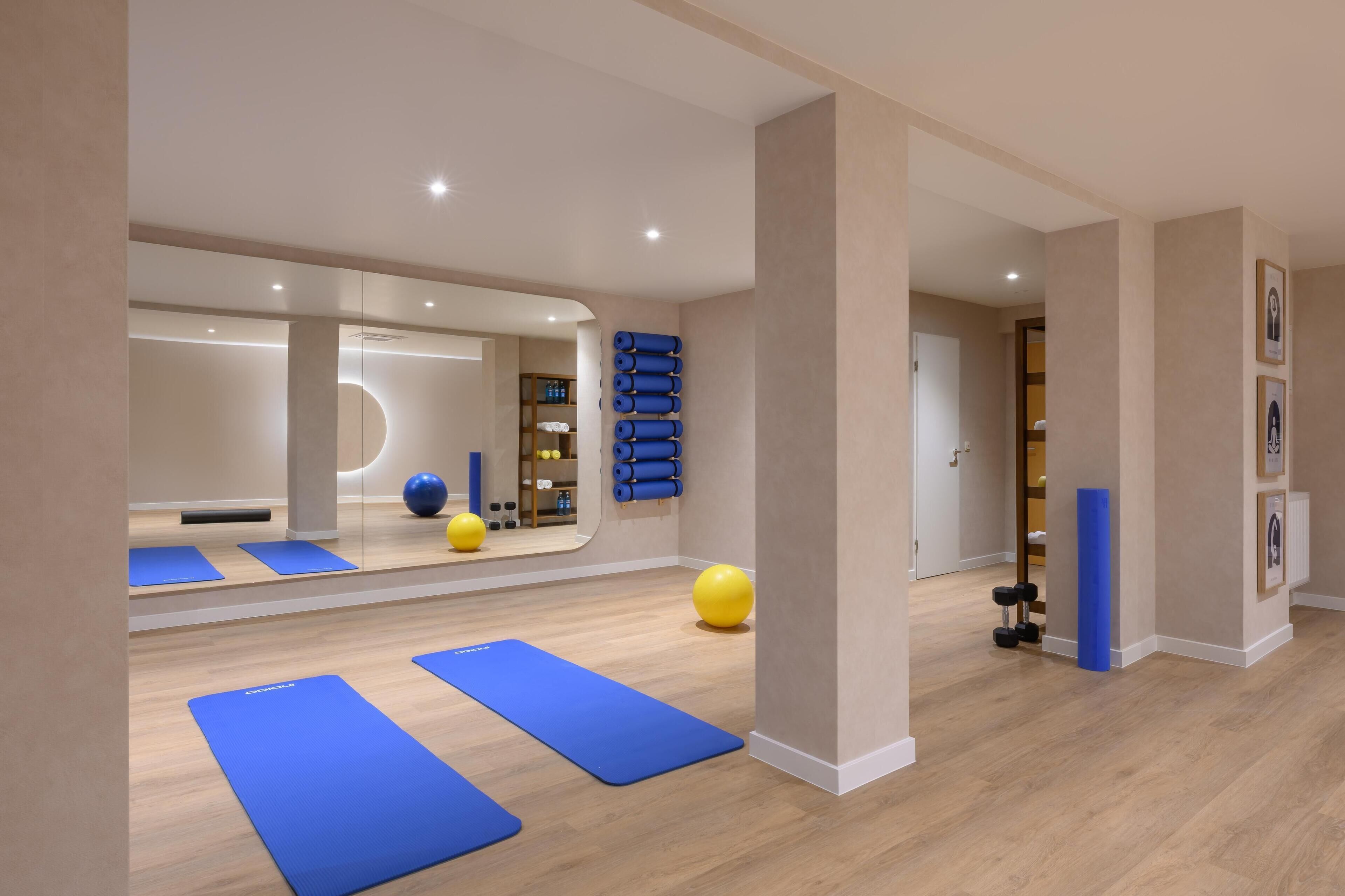 Una habitación amplia con colchonetas de ejercicio, un espejo grande y pelotas de pilates.