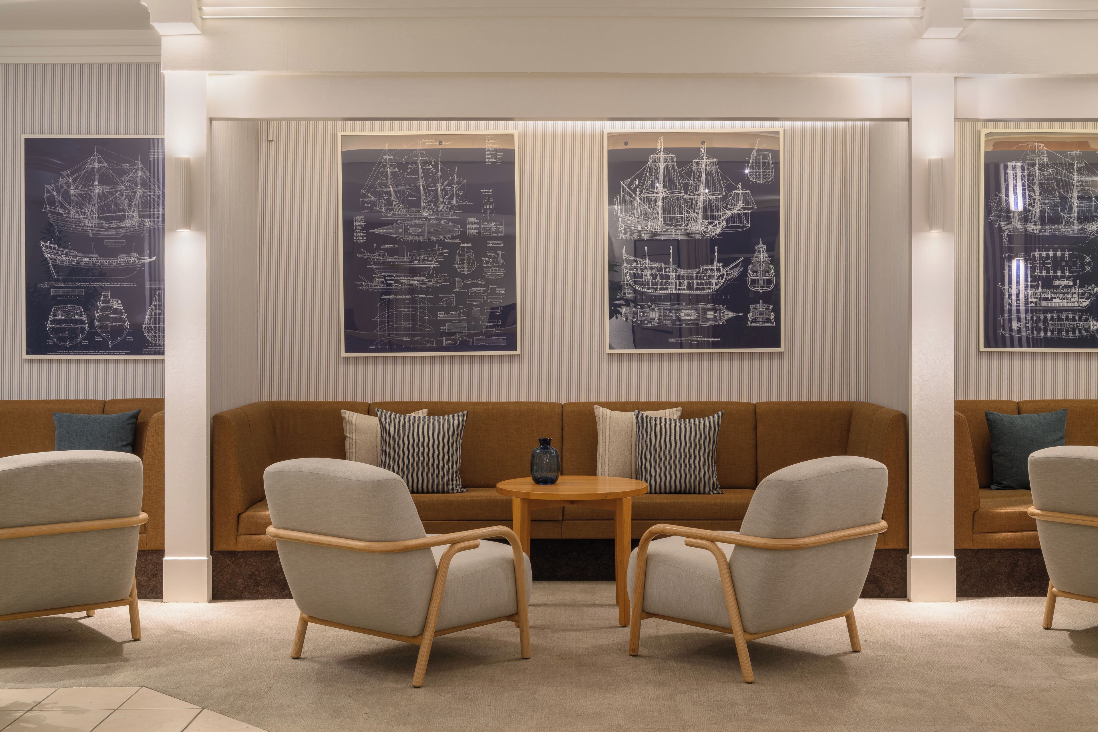 Un salon moderne avec un canapé marron, deux fauteuils et une petite table ronde. Trois grandes reproductions d’architectures, encadrées, ornent le mur.
