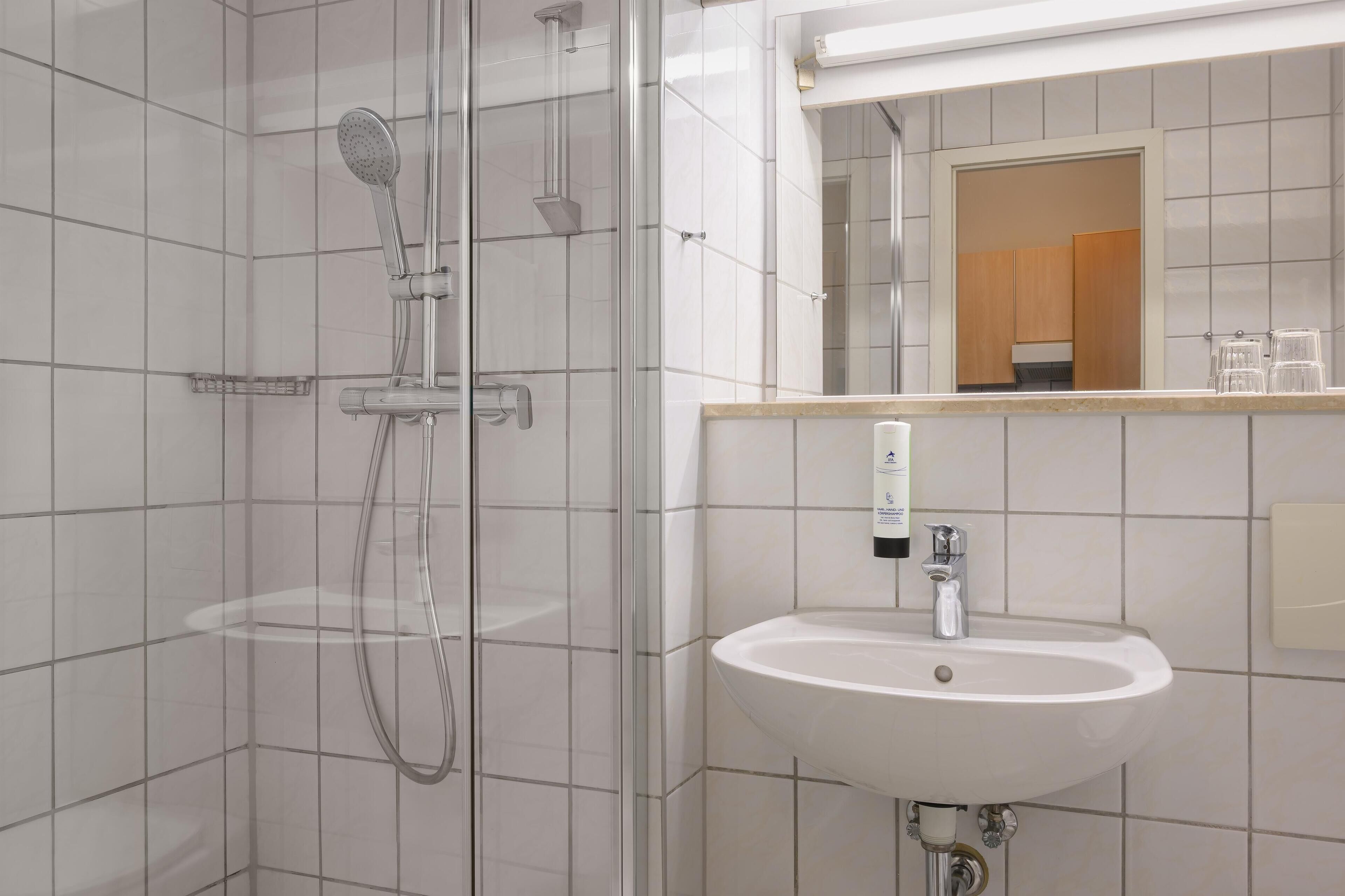 Une salle de bain moderne avec une douche à parois de verre, un lavabo blanc et un miroir au-dessus.