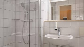 Ein modernes Badezimmer mit einer gläsernen Duschkabine, einem weißen Waschbecken und einem Spiegel darüber.