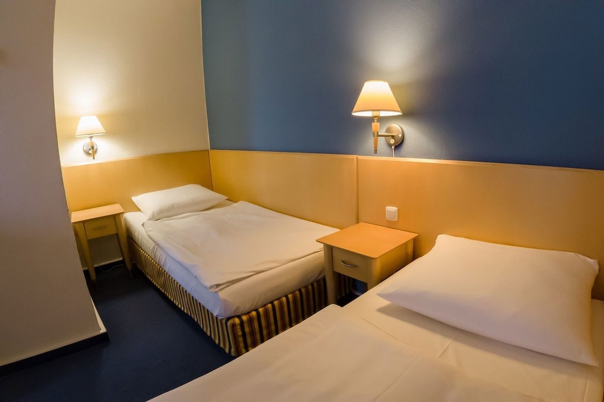 A hotel room with two beds, a nightstand, and wall-mounted lamps.