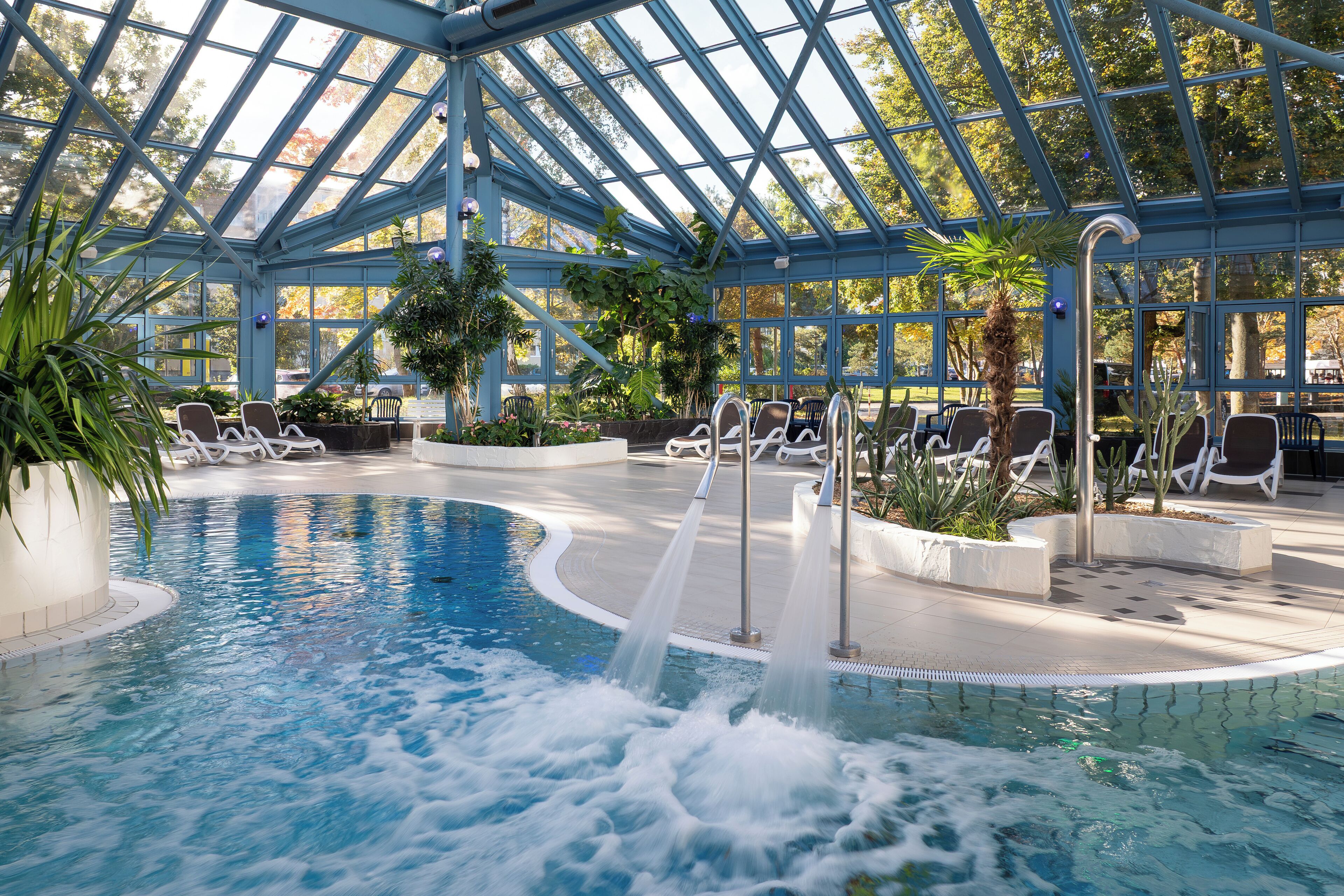 An indoor swimming pool with a glass ceiling, surrounded by lounge chairs and potted plants.