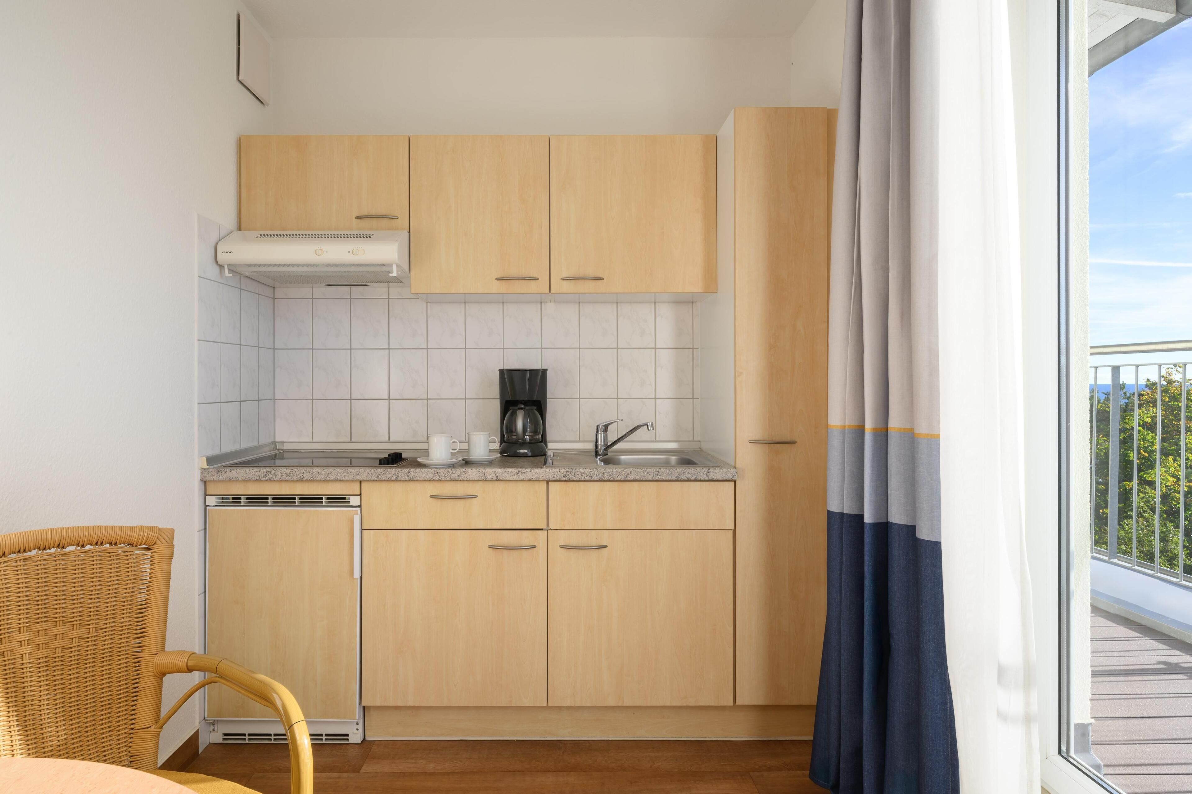 Una cocina compacta con armarios de madera clara, estufa integrada y una ventana con cortinas.