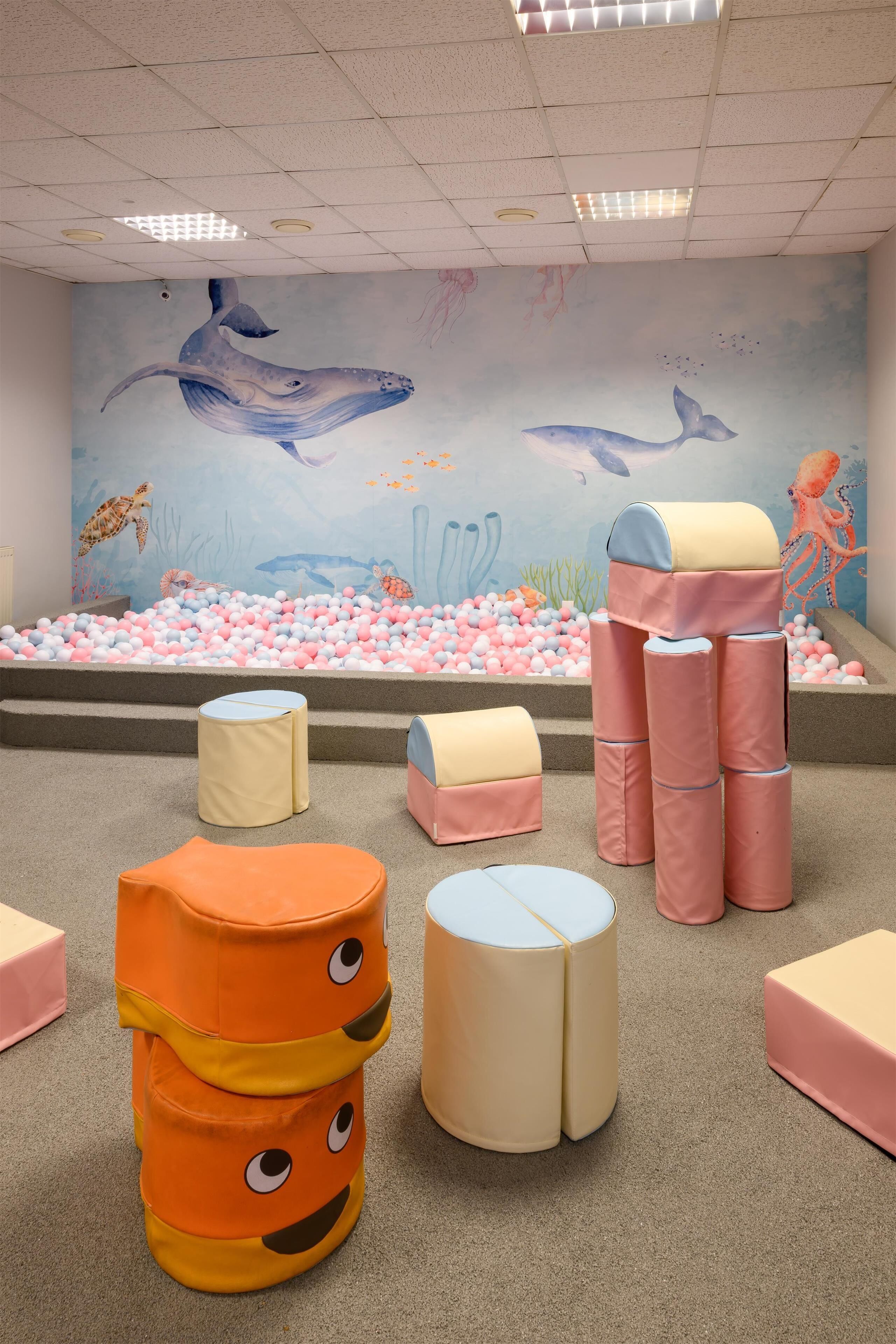 A play area with a ball pit, colorful cushions, and a mural of sea creatures.
