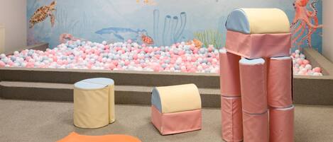 A play area with a ball pit, colorful cushions, and a mural of sea creatures.