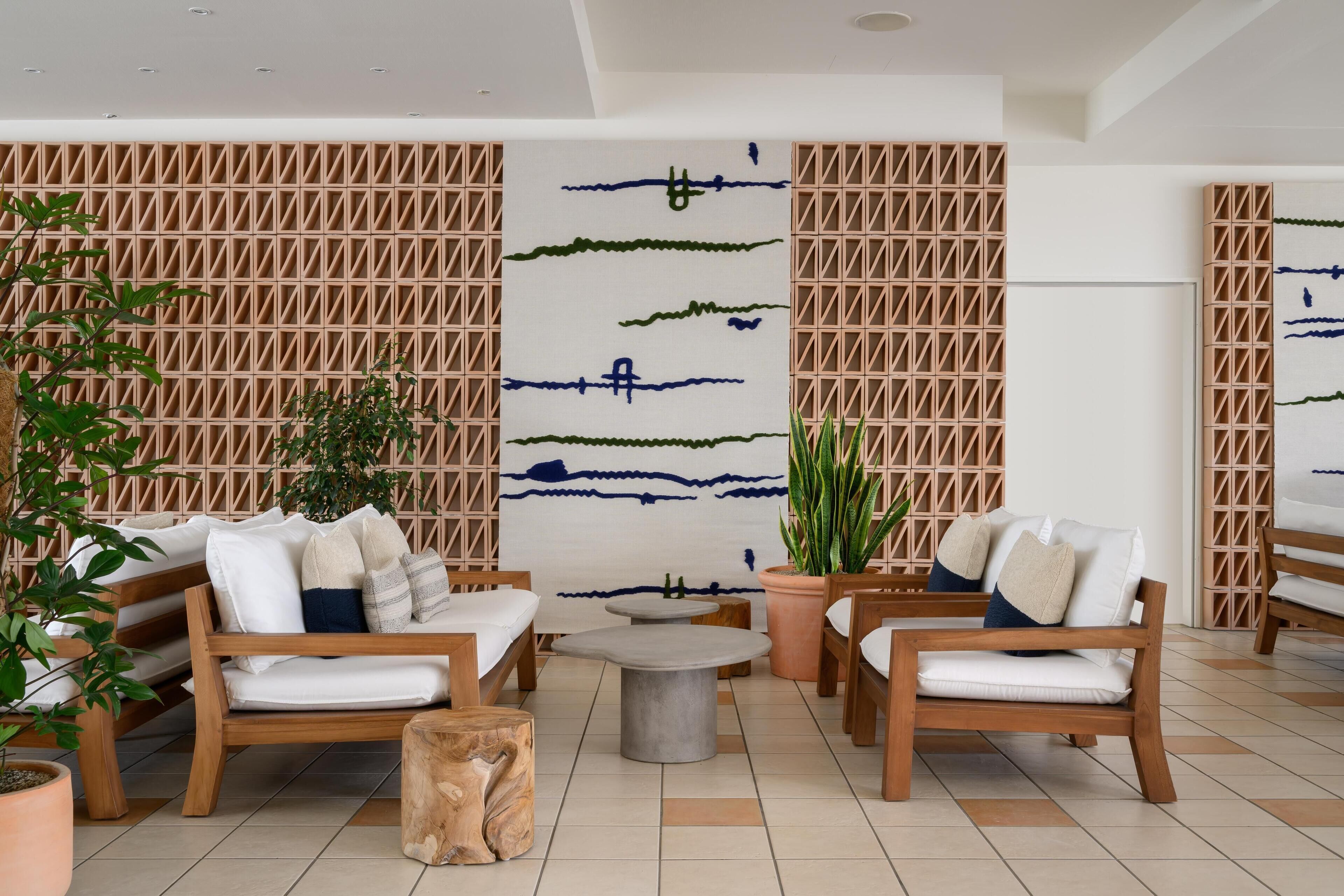 A modern lounge area with wooden furniture, a central round table, and a decorative wall with geometric patterns.
