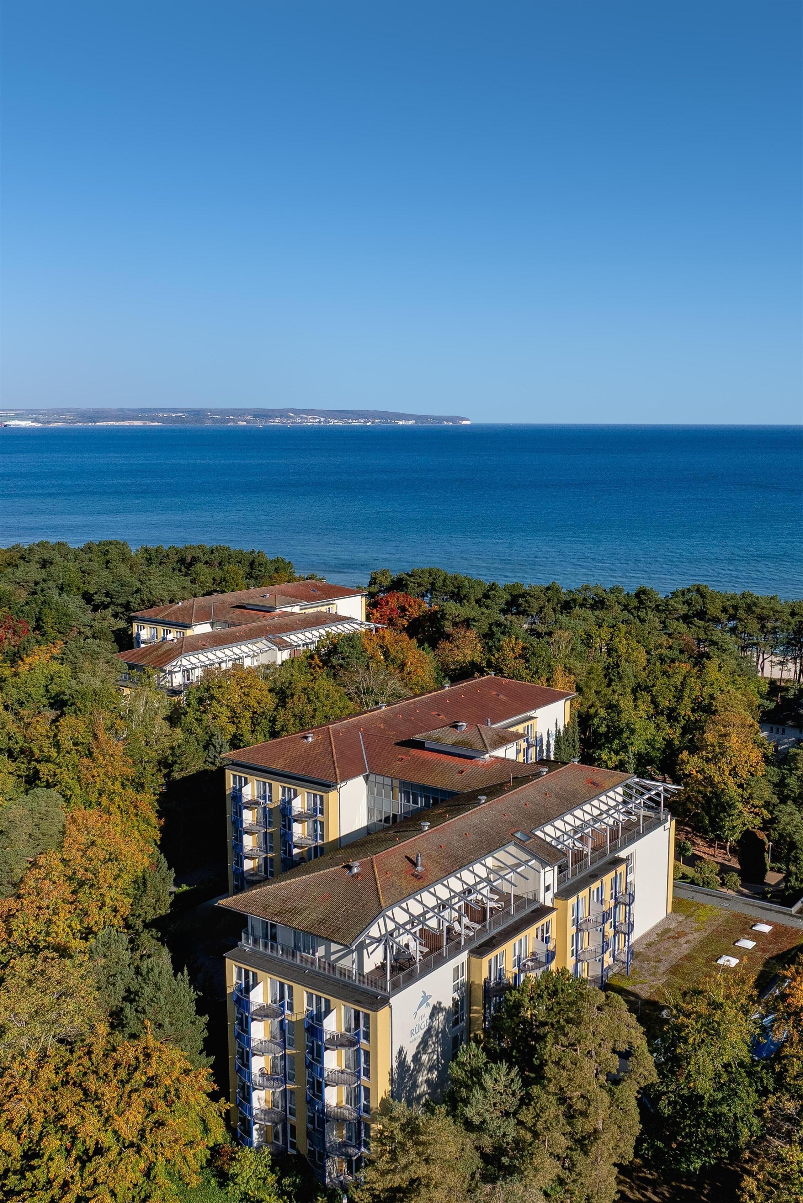 A high-rise hotel with multiple balconies, surrounded by dense trees and overlooking a body of water.