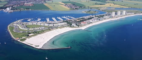 Vista aérea de una zona costera con un puerto deportivo, una playa y un pueblo.
