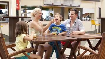 Eine Familie speist in einem Freiluftrestaurant mit Holztisch und -stühlen.