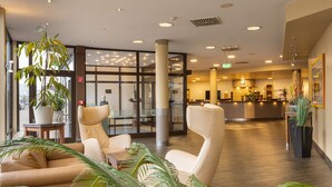 A spacious lobby with leather seating, a reception desk, and potted plants. - IFA Fehmarn Hotel & Ferien-Centrum (Fehmarn)