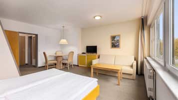 Ein Hotelzimmer mit einem Bett, einem Sofa, einem Schreibtisch, einem Sessel, einem Fernseher und einem Fenster.