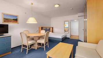 A hotel room with a bed, a desk with chairs, a TV, a lamp, and a wardrobe.