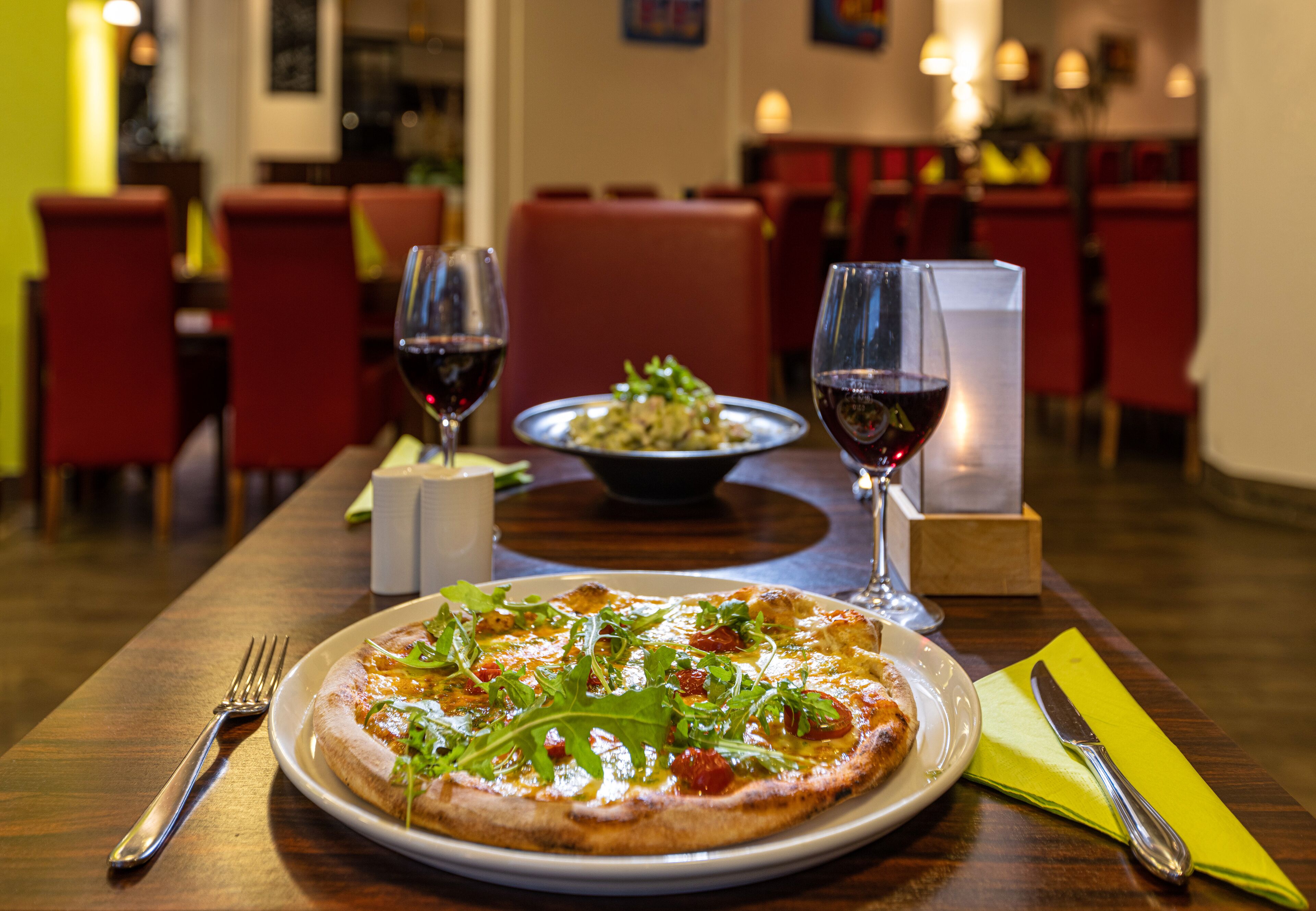 Une scène de restaurant avec une pizza et des verres à vin sur une table.