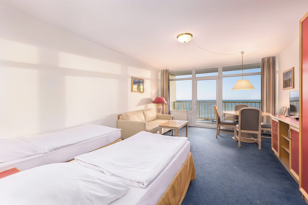 Habitación de hotel con dos camas, un escritorio, una silla y vista al mar.