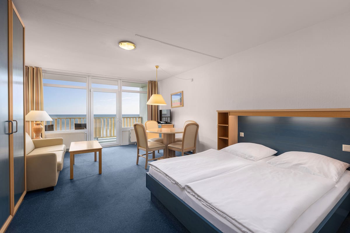 Habitación de hotel con cama, escritorio, sillón, sofá y vista al mar.