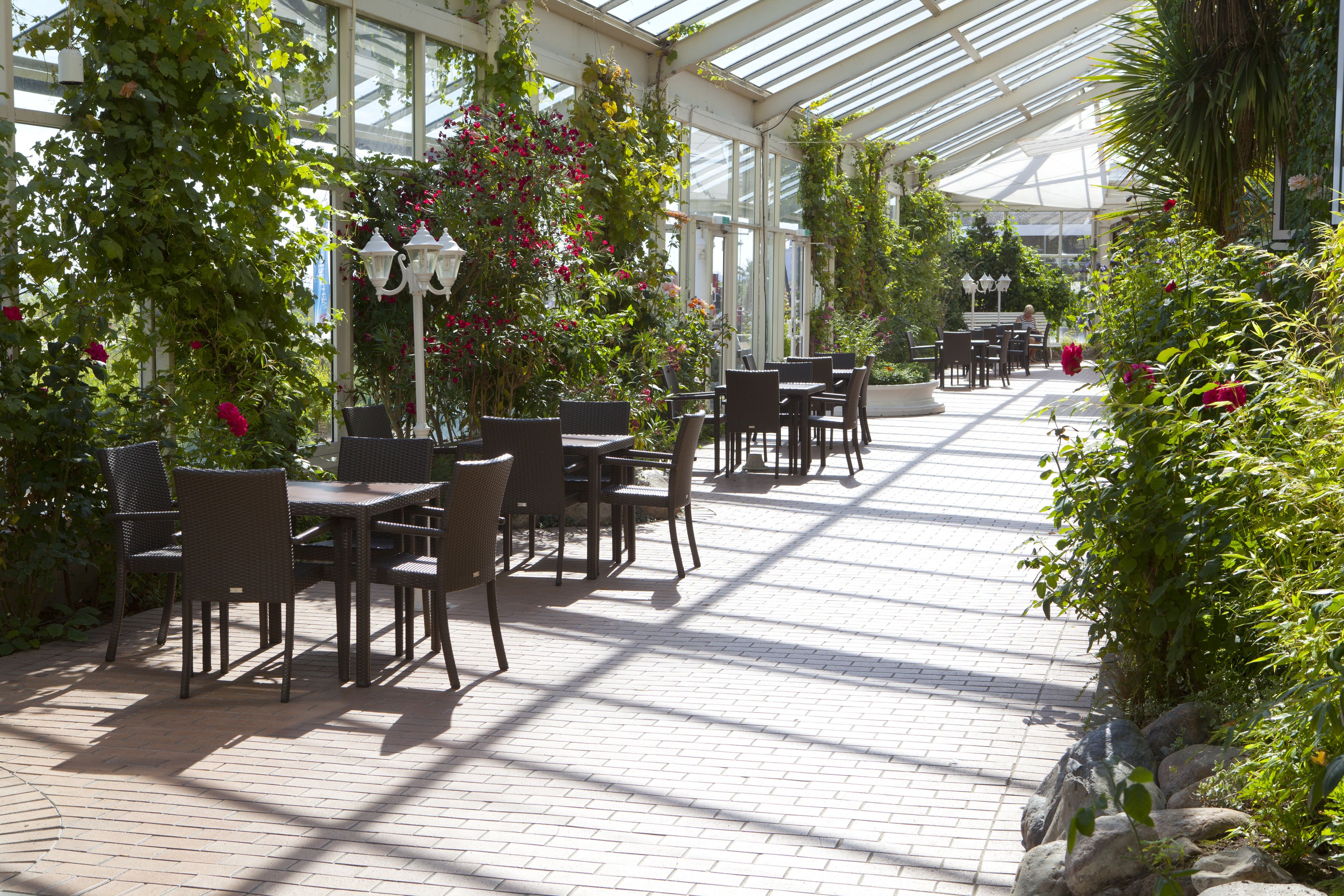 An indoor garden with tables and chairs, surrounded by lush greenery and flowers.