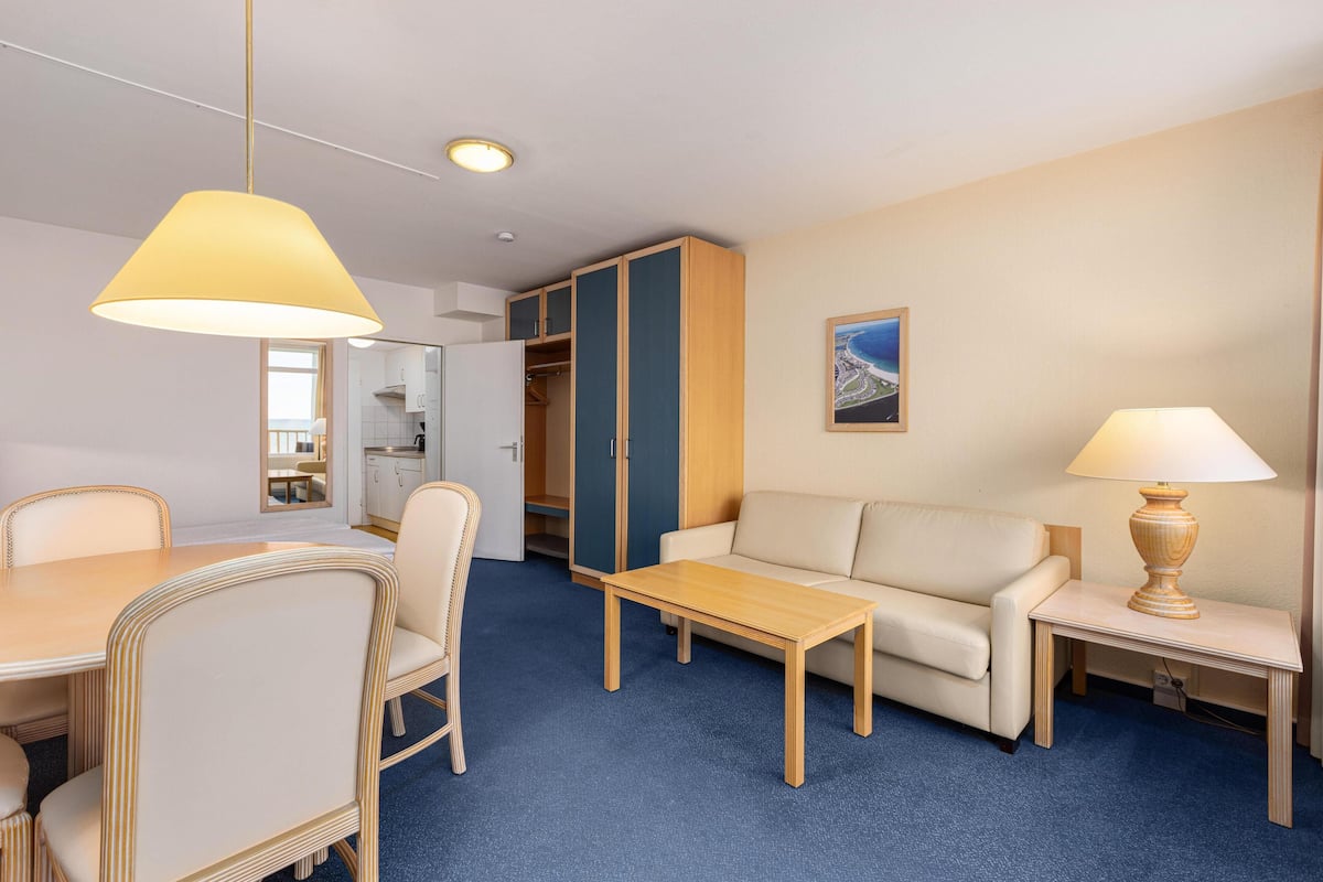 Habitación de hotel con una mesa de comedor, sillas, un sofá, una mesa de centro, una lámpara, un armario y un cuadro en la pared.