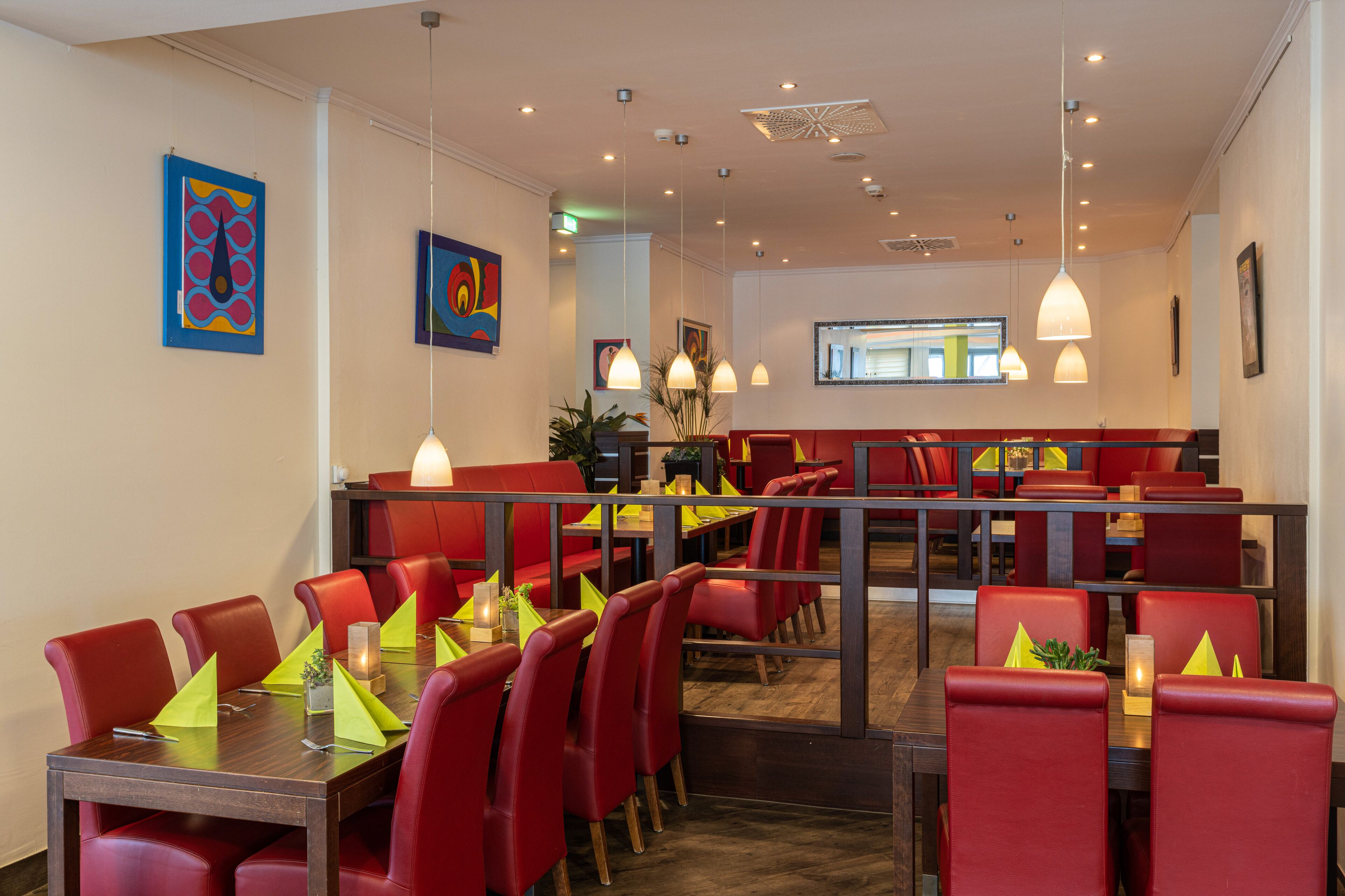 A restaurant with red seating, multiple pendant lights, and artwork on the walls.