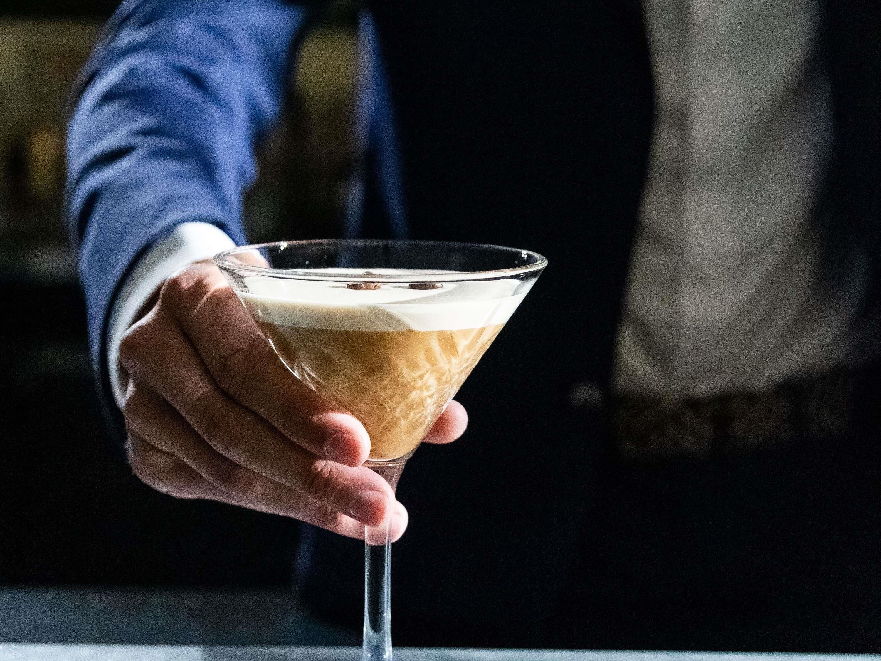 A hand holding a martini glass with a layered drink.