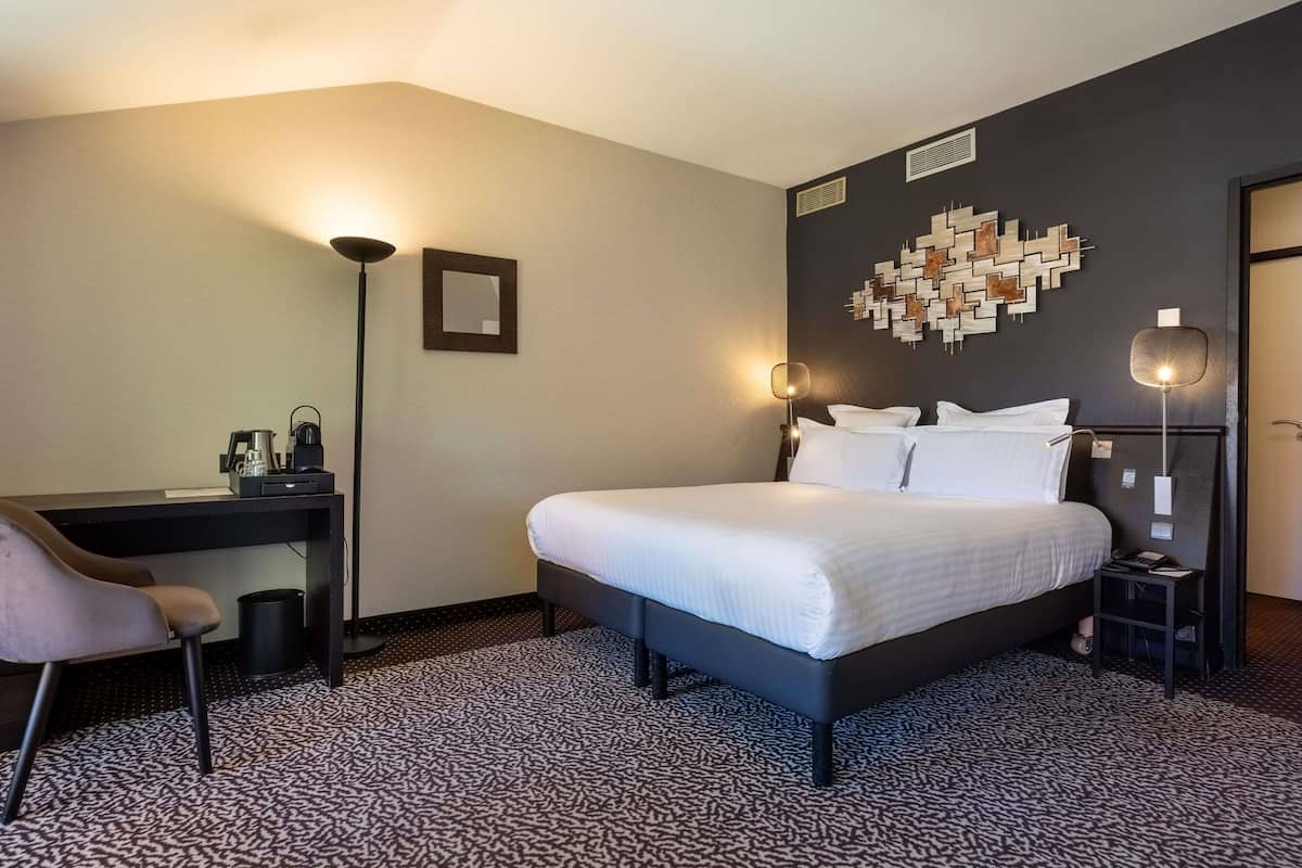 A hotel room with a bed, a desk, a chair, and a wall-mounted artwork.