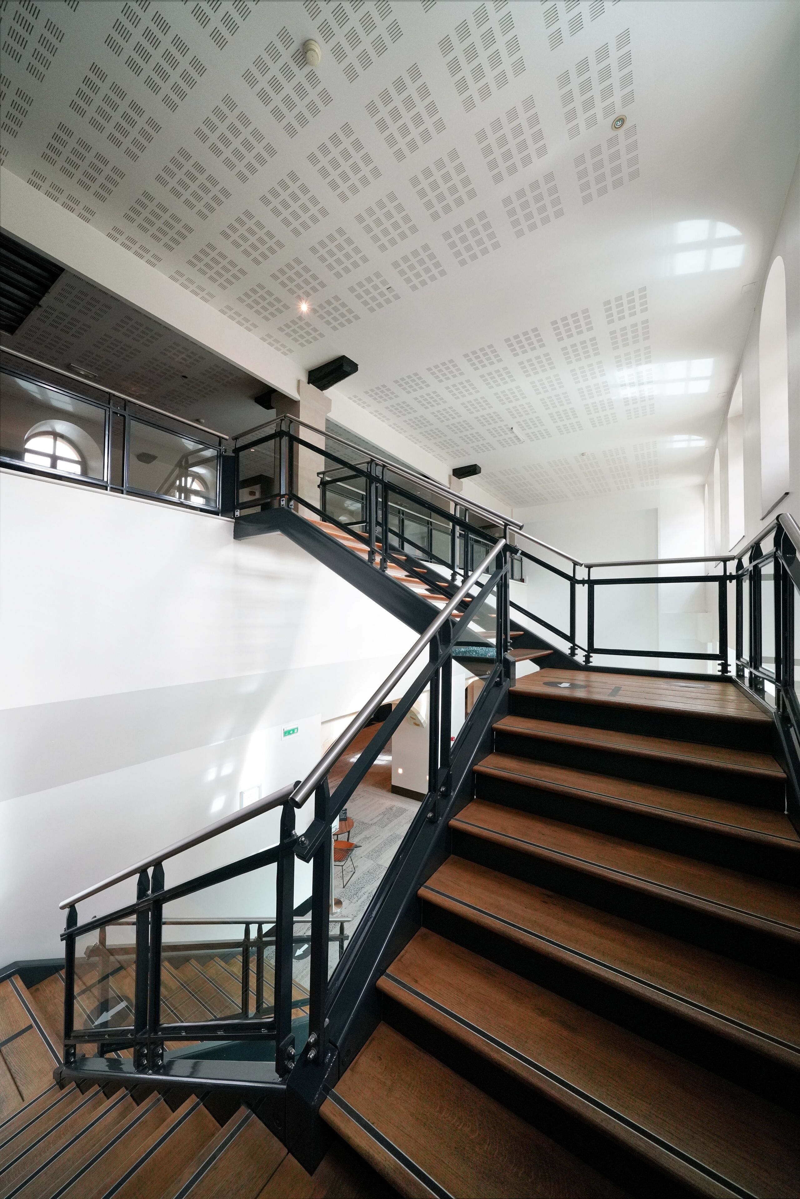 Un escalier avec des marches en bois et des rampes en métal, situé dans un bâtiment moderne.