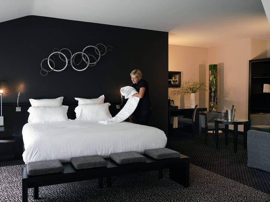 A modern hotel room with a large bed, a bench, a desk, and a chair.