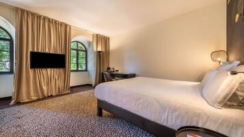 A hotel room with a bed, a desk, a chair, a TV, and a window with curtains.