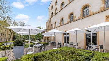 Un patio con mobiliario exterior, una estatua y un edificio con ventanas de arco.