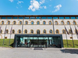 Un edificio de grandes dimensiones con un estilo arquitectónico clásico, que presenta múltiples ventanas en arco y una entrada destacada con puertas de vidrio.