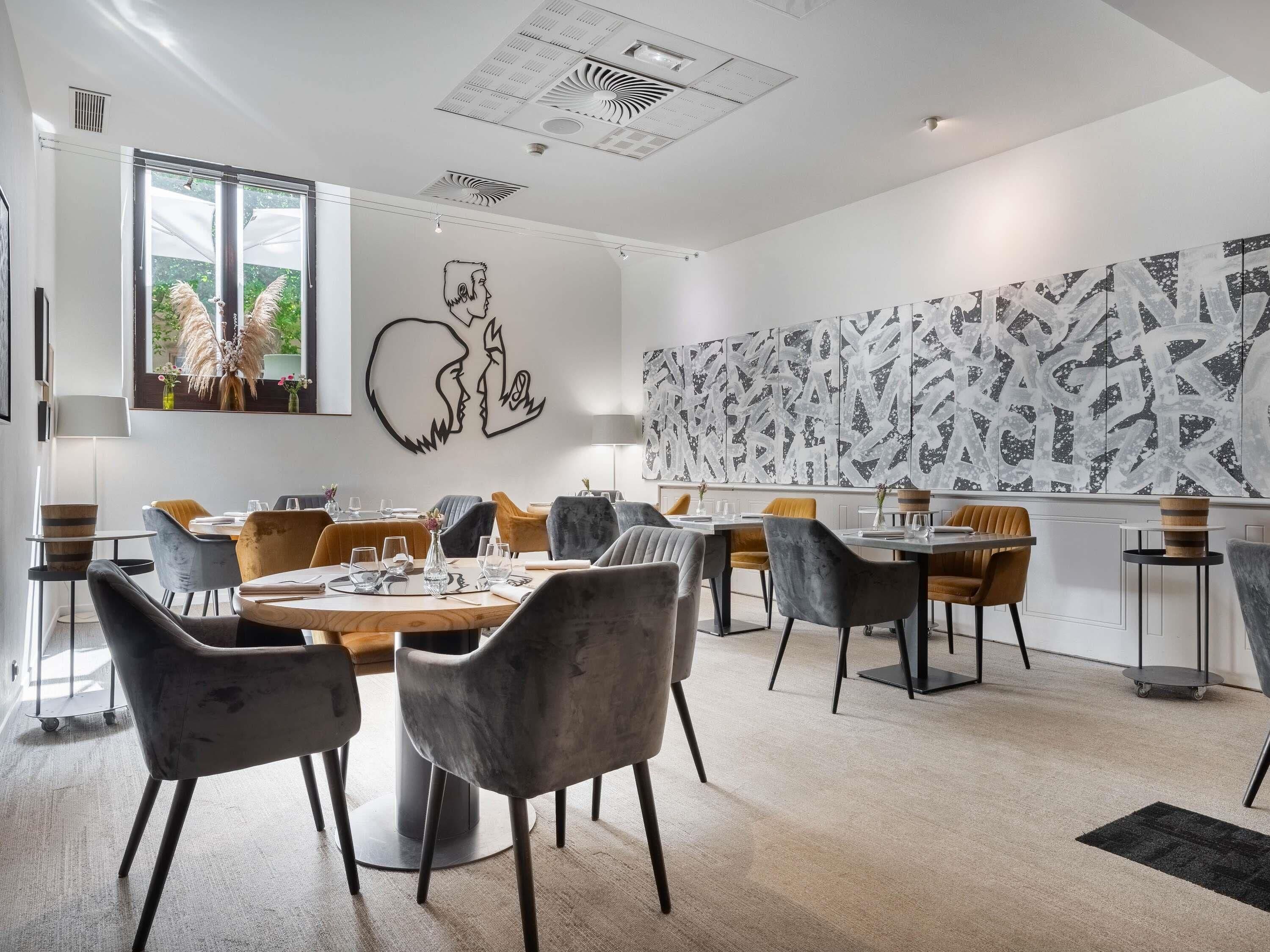 Un comedor moderno con mesas redondas, sillas grises y amarillas, y arte abstracto en la pared.