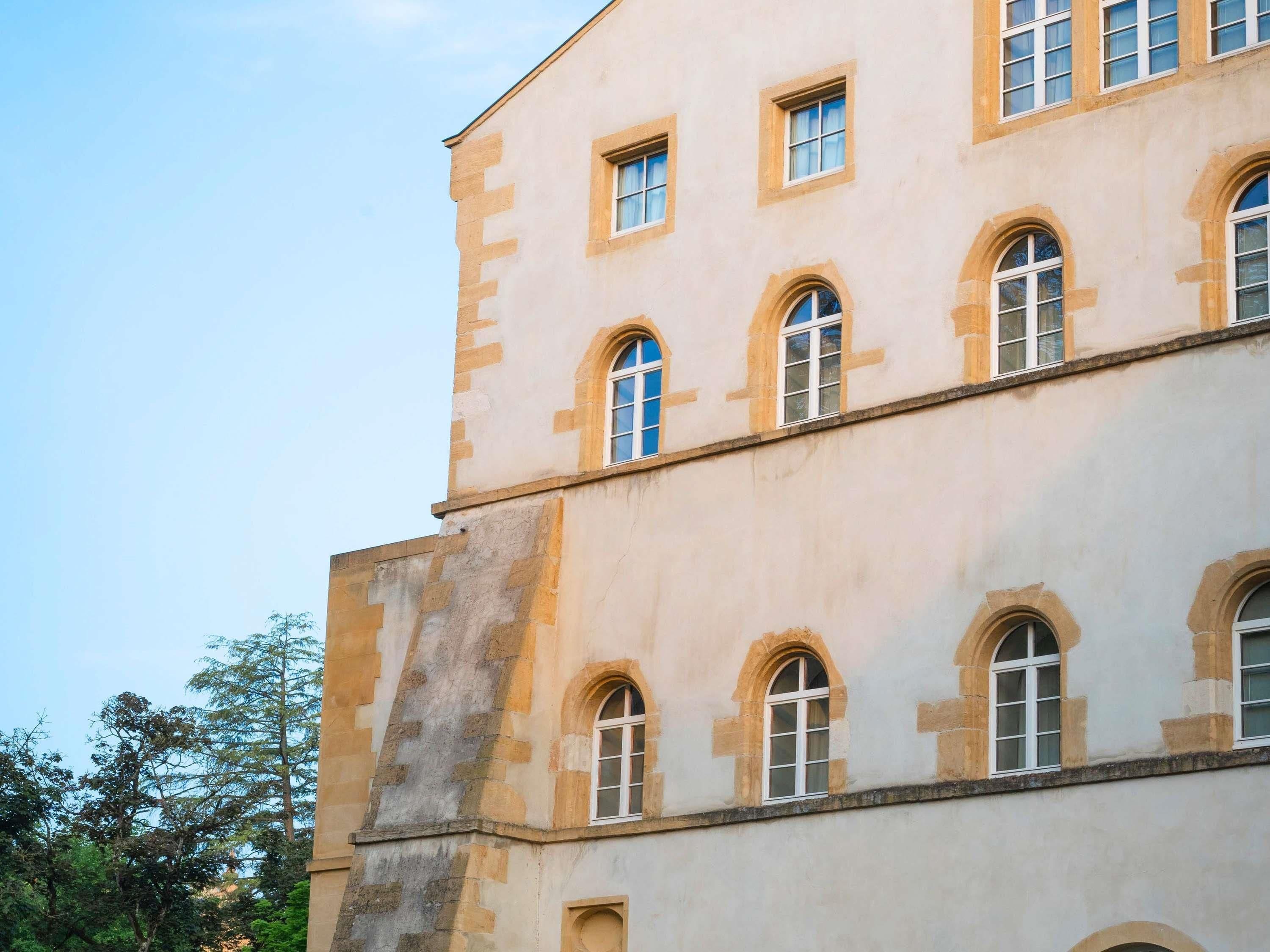 Ein mehrstöckiges Gebäude mit einer symmetrischen Fassade, das gleichmäßig verteilte Fenster und einen zentralen Eingang aufweist.