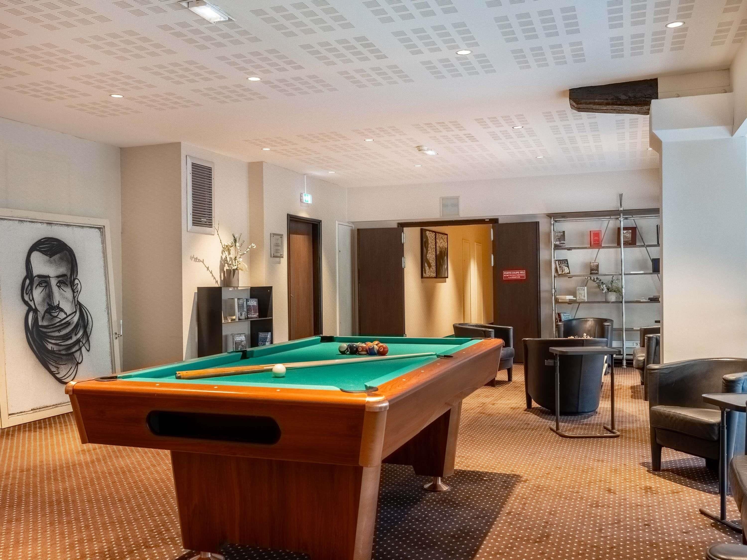A pool table in a room with a ceiling with recessed lighting, a bookshelf, and a door with a sign.
