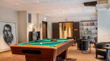 A pool table in a room with a ceiling with recessed lighting, a bookshelf, and a door with a sign.