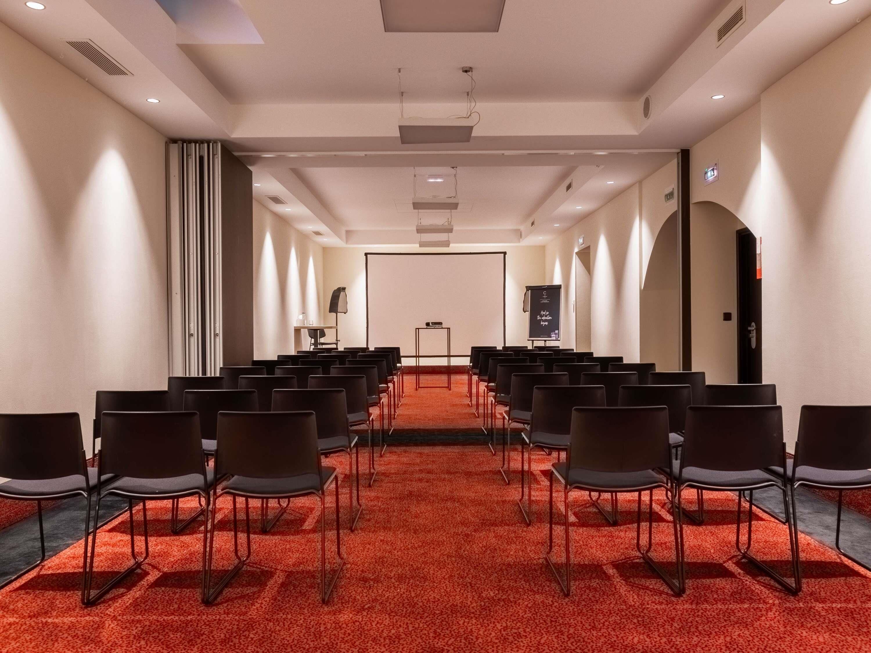 A conference room with rows of chairs, a projector screen, and a carpeted floor.