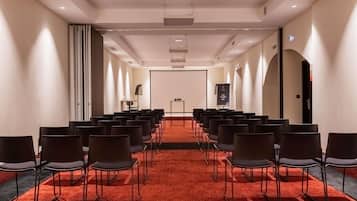 A conference room with rows of chairs, a projector screen, and a carpeted floor.