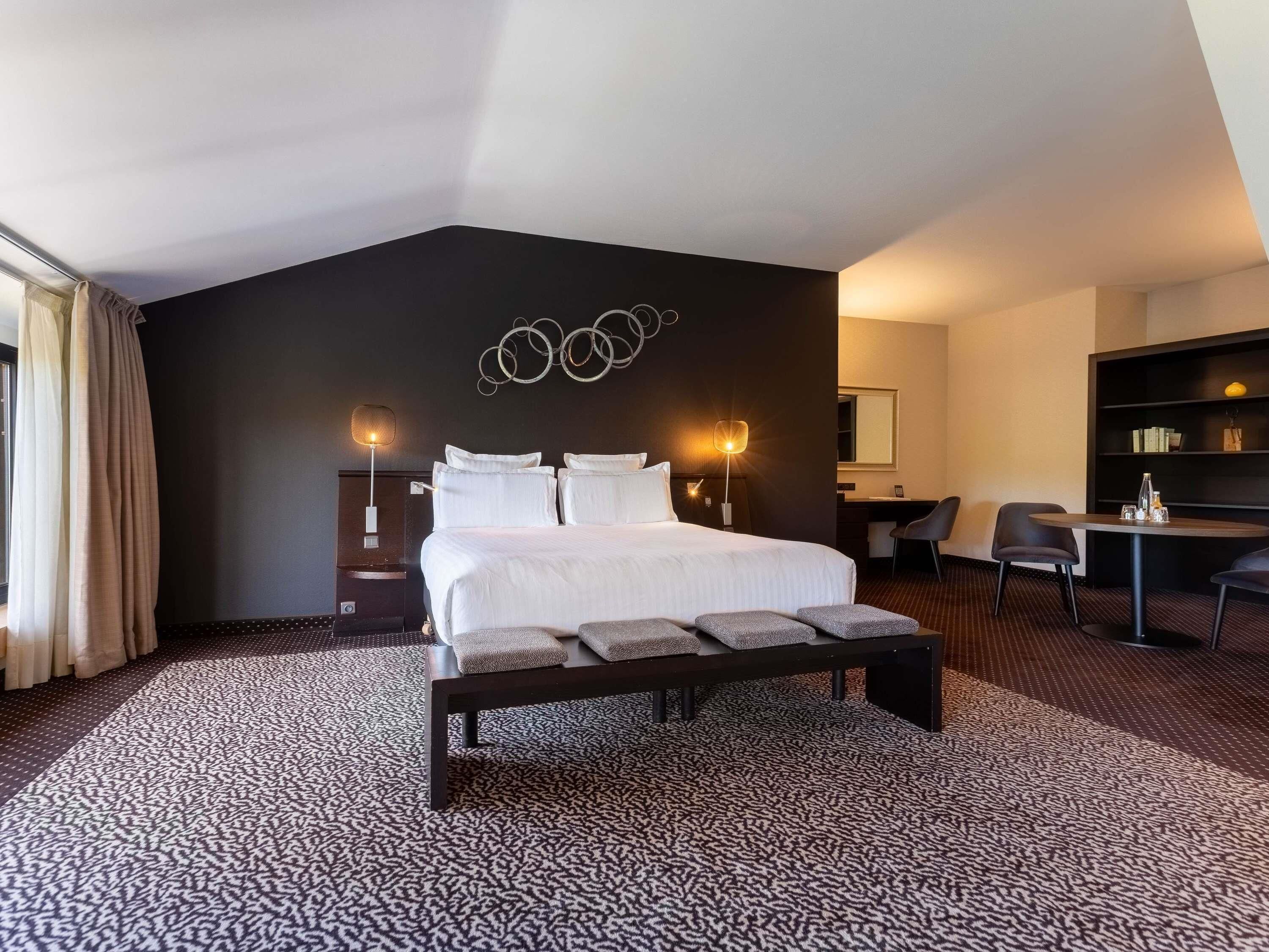 Una habitación de hotel con una cama grande, un escritorio, una silla, un banco y una estantería.