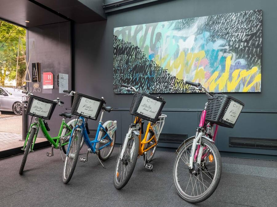 A row of bicycles with baskets, a large abstract painting, and a car parked outside.