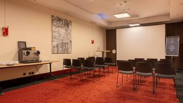 A conference room with a red carpet, a coffee machine, a projector screen, and a large abstract painting on the wall.