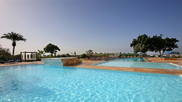 A large outdoor swimming pool with clear blue water, surrounded by palm trees and lounge chairs. - Anezi Tower Hotel (Agadir)