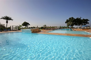 A large outdoor swimming pool with clear blue water, surrounded by palm trees and lounge chairs. - Anezi Tower Hotel (Agadir)