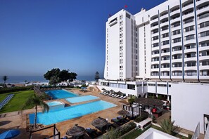 Un hôtel doté d’un espace piscine, comprenant des chaises longues et des parasols, et offrant une vue sur l’océan.