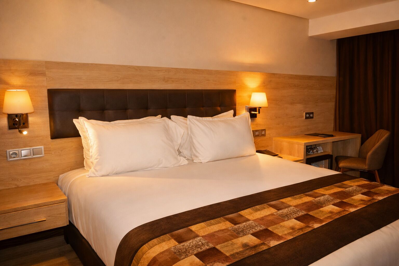 A hotel room with a large bed, two bedside lamps, a desk, and a chair.