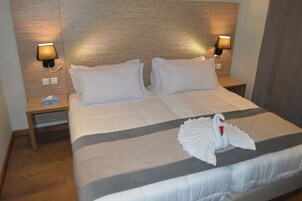 Una cama bien hecha con sábanas blancas, dos lámparas de noche y una toalla con forma de cisne sobre la cama.